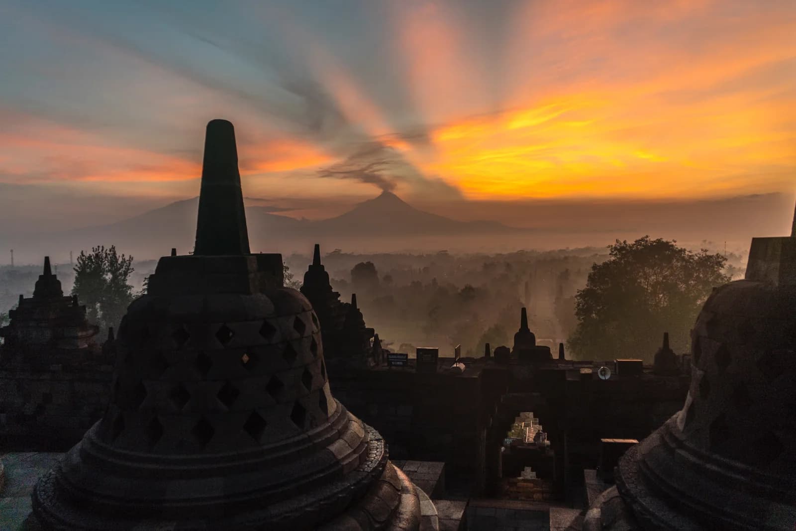 Borobudur stupas against an orange dawn sky and distant mountains