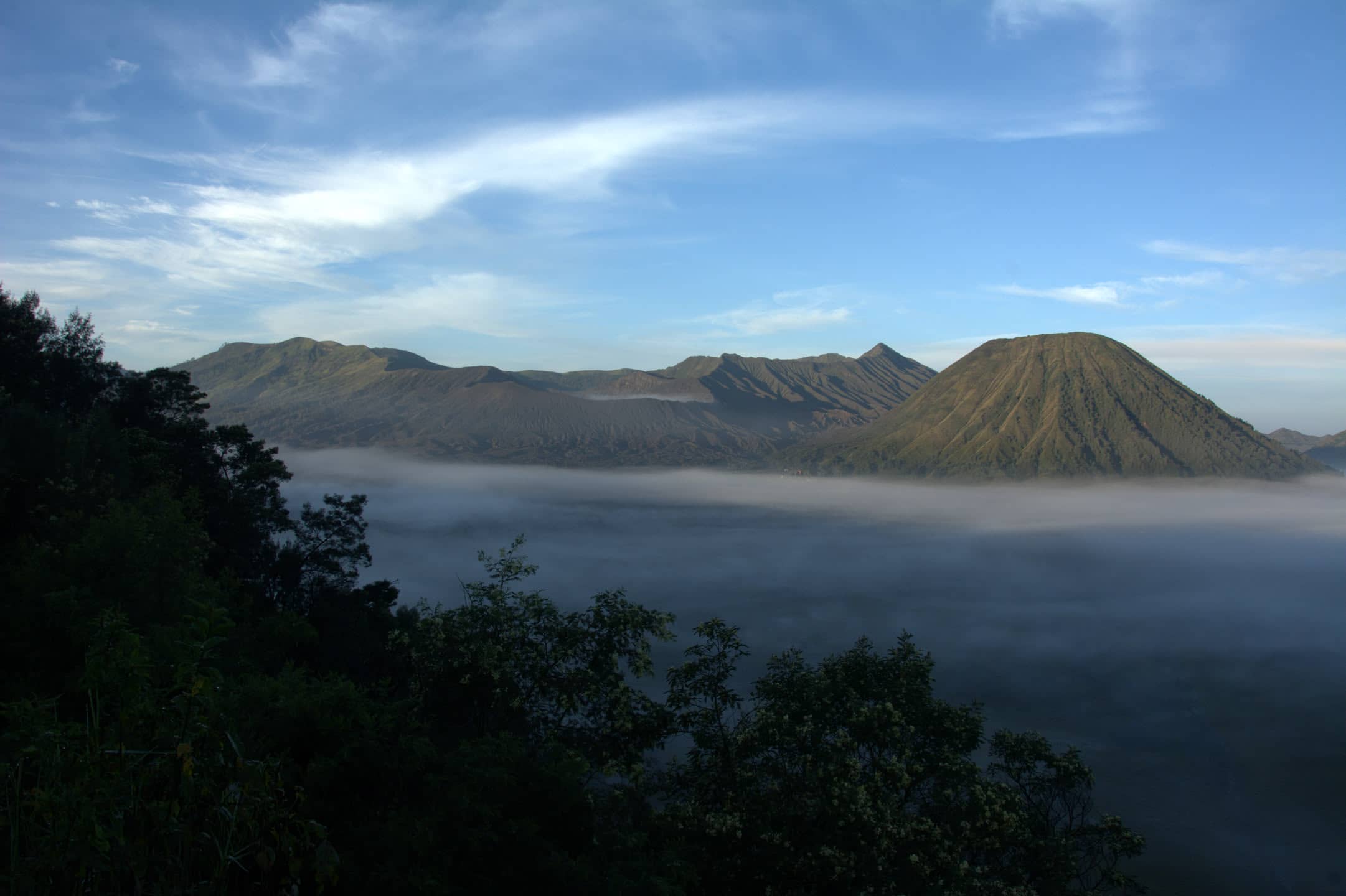 Tengger caldera at dawn: the Batok cone and the smoking Bromo crater above a sea of fog