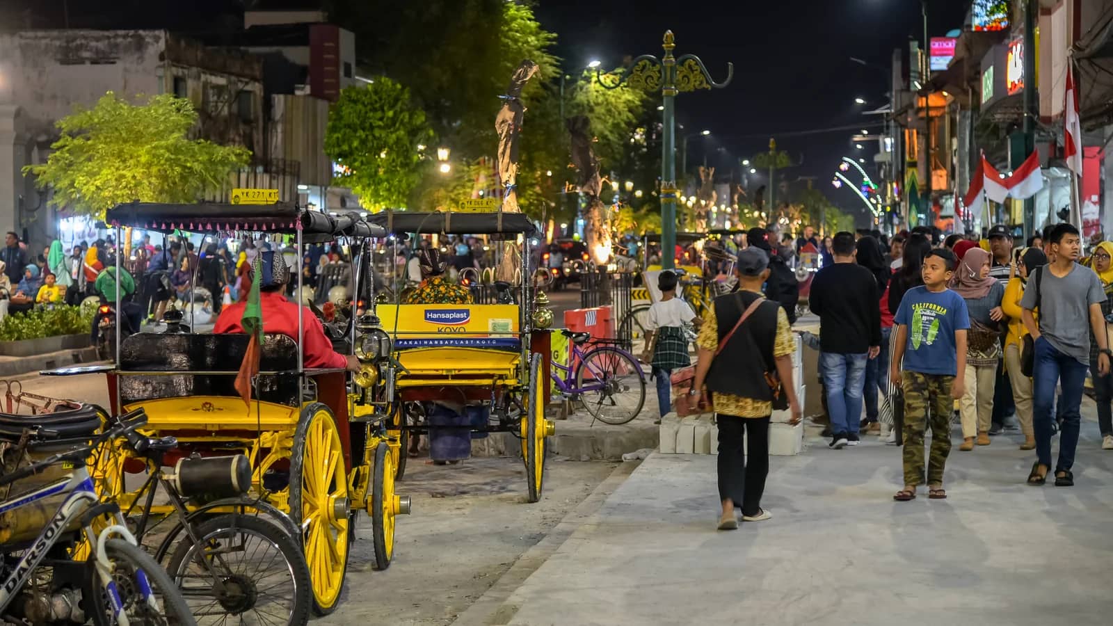 Pedestrians and yellow cycle rickshaws on Malioboro street in Yogyakarta at night