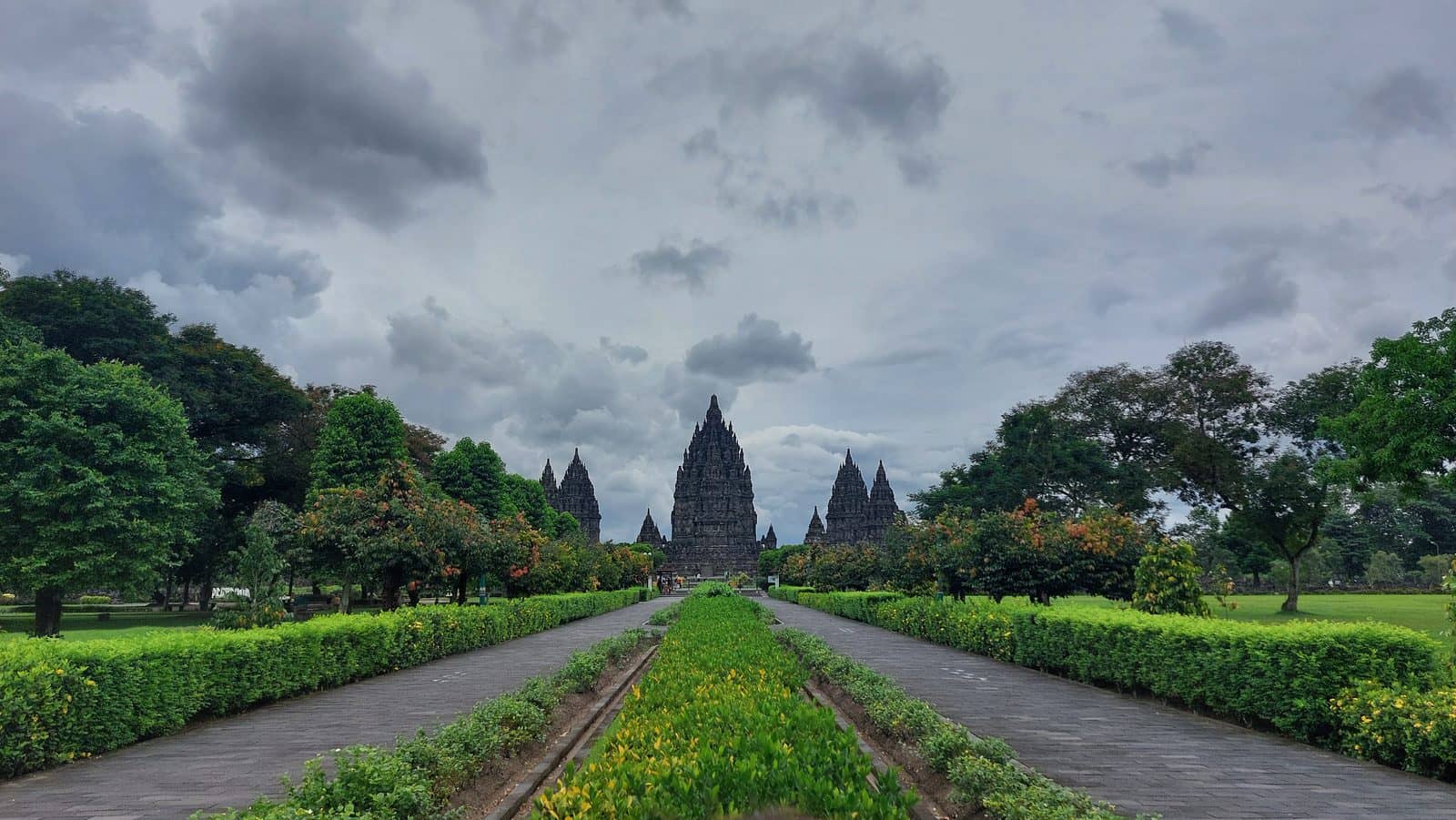 The Prambanan temple complex near Yogyakarta: stone towers at the end of a garden path under a cloudy sky
