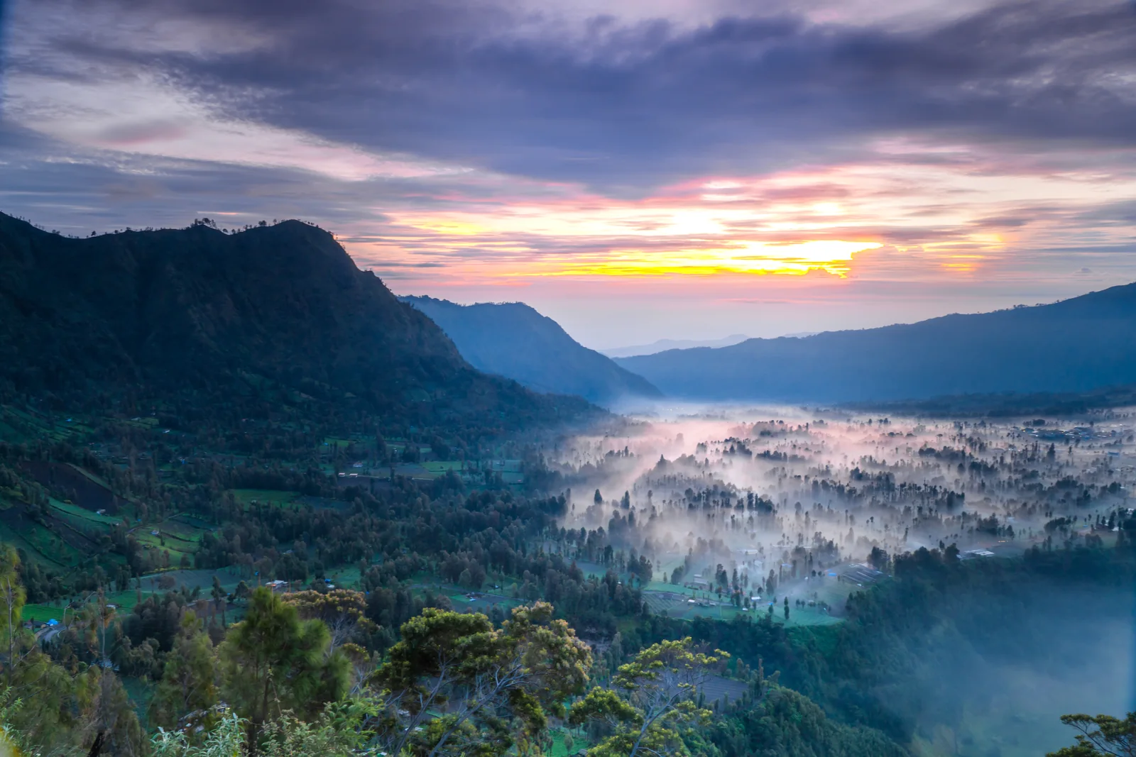Sunrise above a wooded valley and fields in mist, seen from Seruni