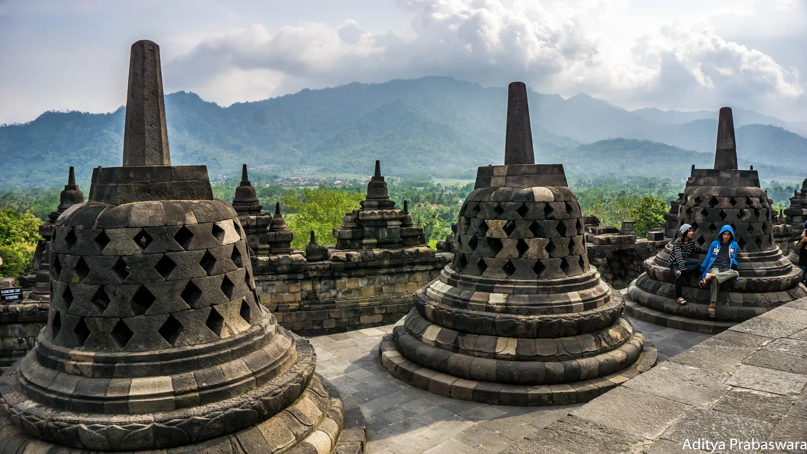 Perforated stone stupas on Borobudur's upper terrace with mountains and clouds behind them