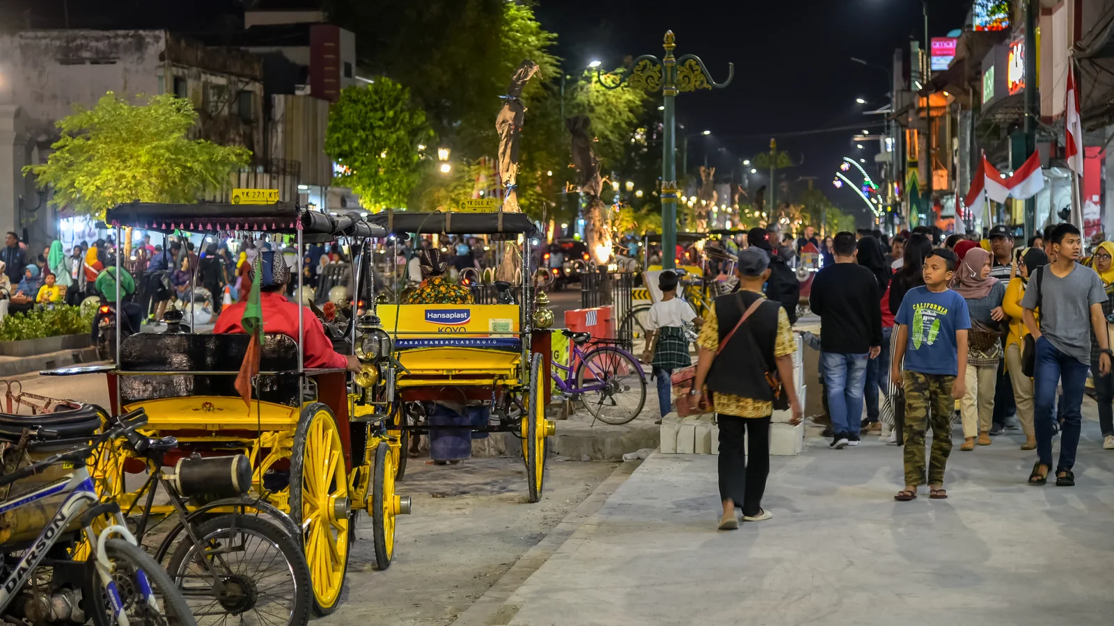 Pedestrians and yellow cycle rickshaws on Malioboro street in Yogyakarta at night