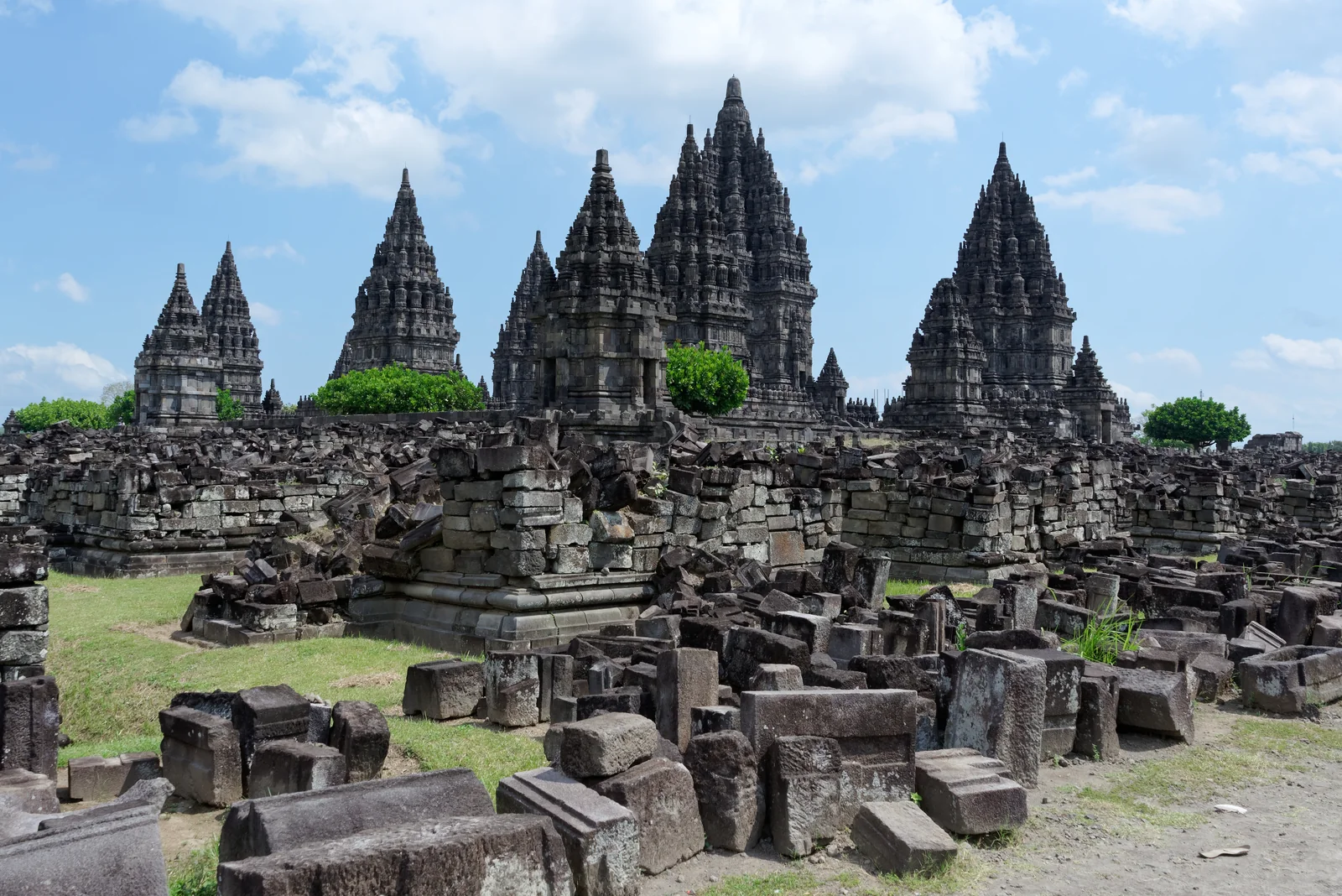 Prambanan's stone temple towers with remains of smaller structures in the foreground